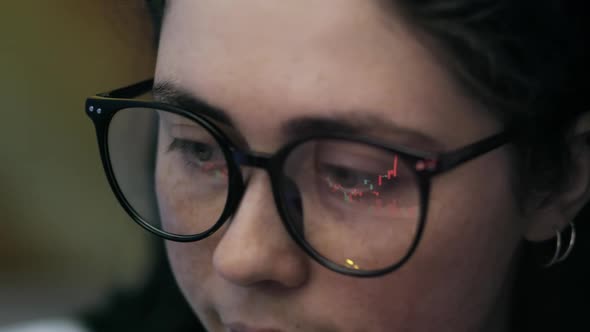 Close up a woman trader wearing eyeglasses looking at a computer screen with trading charts