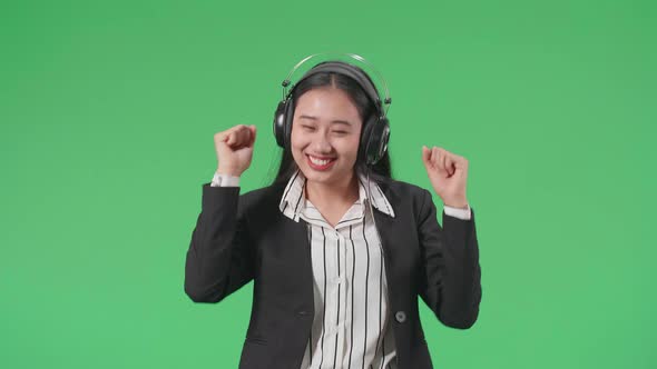 An Asian Business Woman Listening To Music With Headphones And Dancing In The Green Screen Studio