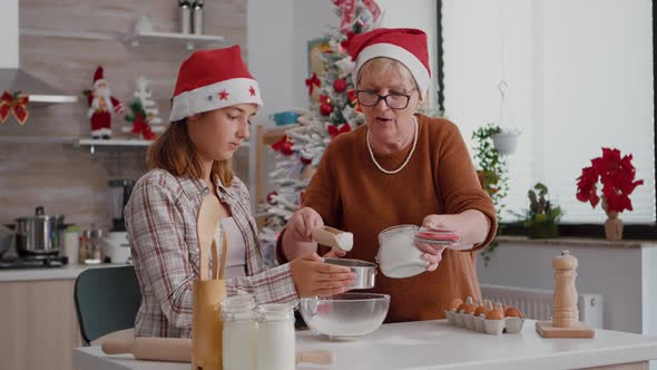 Senior Woman Putting Flour in Metalic Siev While Granddaughter Sift Ingredient in Bowl