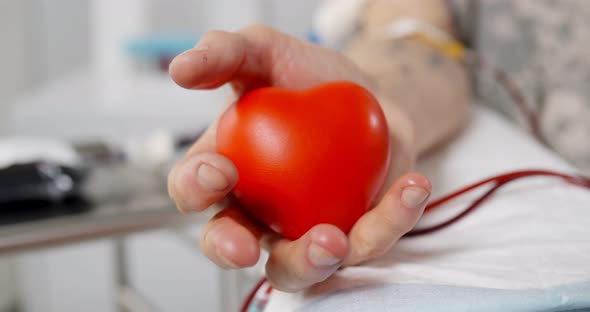 Close Up of Blood Donor Squeezing Rubber Bulb in Form of Heart in Hand