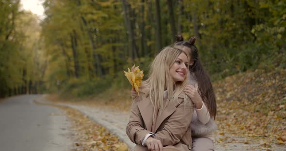 Stylish Mother and Daughter Sitting in Autumn Park