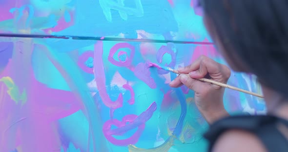 Tight shot of a woman painting a purple heart on a big cloth canvas in a public park