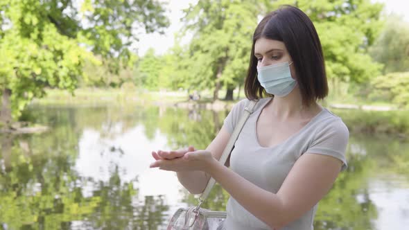 A Young Caucasian Woman in a Face Mask Applies Disinfection Gel on Her Hands