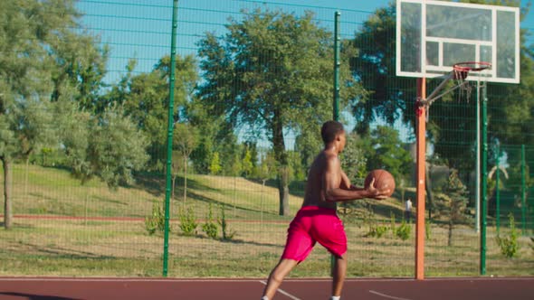 Shirtless Basketball Player Slam Dunking at Court