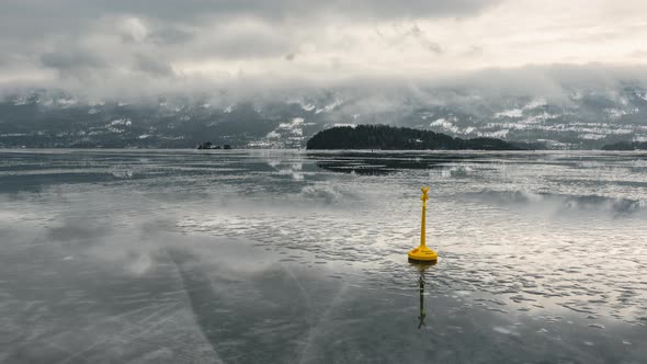 Calm Icy Steinsfjorden In Vik, Norway With Yellow Lake Buoy And Reflections Of Clouds Soaring Above.