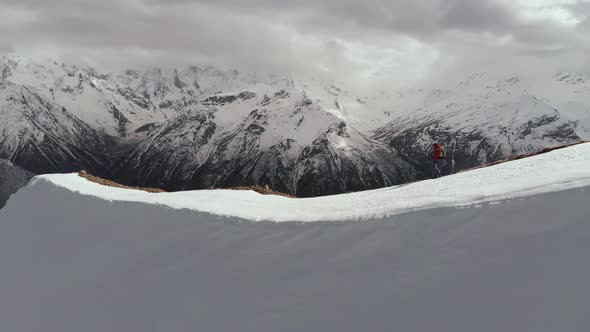 Aerial View Young Man in Sunglasses with a Backpack Goes Down the Mountain on the Crest on the