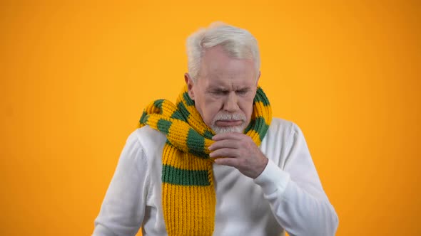 Ill Elderly Man in Scarf Coughing Against Orange Background, Bronchitis Symptom