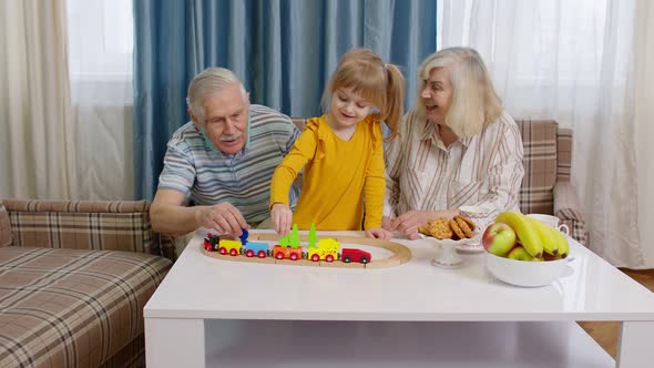 Mature Couple Grandmother Grandfather with Child Girl Grandkid Riding Toy Train on Railroad at Home