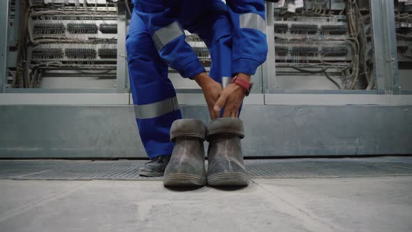 Electrical technician is putting on special protective shoes. Electrician wears rubber boots.