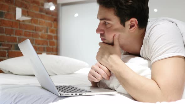 Thinking Pensive Man in Bed Working on Laptop at Night