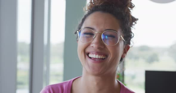 Portrait of smiling biracial creative businesswoman wearing glasses in modern office interior