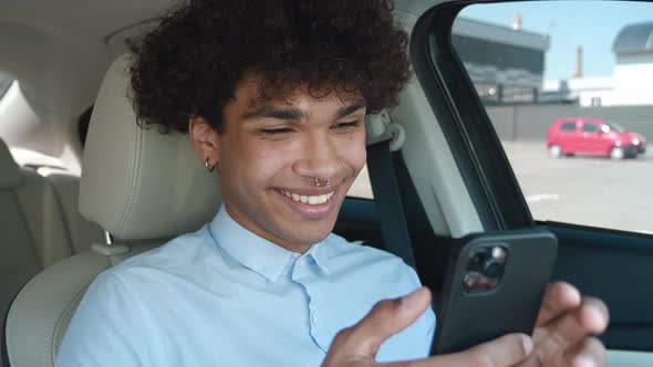 Young Curlyhaired Mixed Race Guy Reading News on the Internet Playing Games on His Smartphone