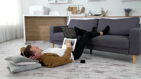 Young man using laptop at home, lying on the floor