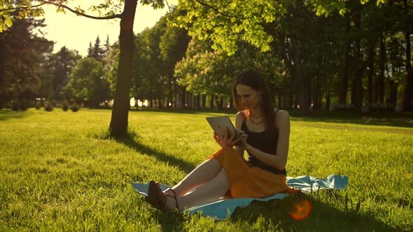 Cheerful, Young Woman Browsing Her Tablet in the Park.