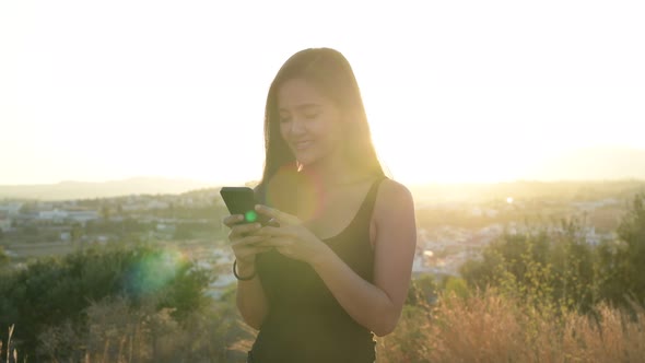 Young Happy Asian Tourist Woman Thinking While Using Phone On The Hill