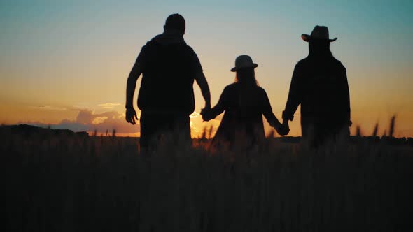 Silhouette Family Farmers Working in a Wheat Field at Sunset. Young Parents with Their Daughter in a