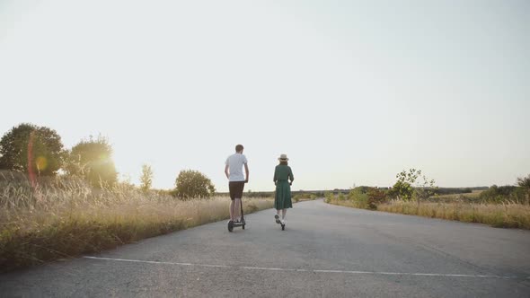 Back View of Couple in Love Riding Together on Electric Scooters on Asphalt Road