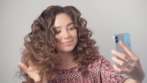A girl with long dark curly hair takes a selfie with a modern smartphone
