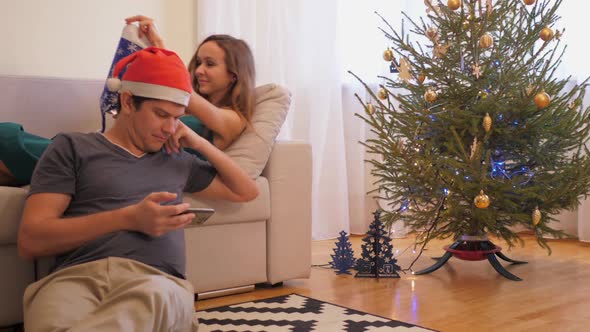 Woman Puts on Christmas Hat While Man Reads News on Gadget