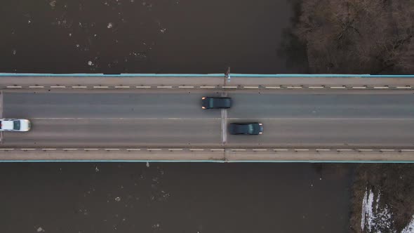A Bridge Across a Muddy River Stream with Floating Ice Floes Cars are Driving