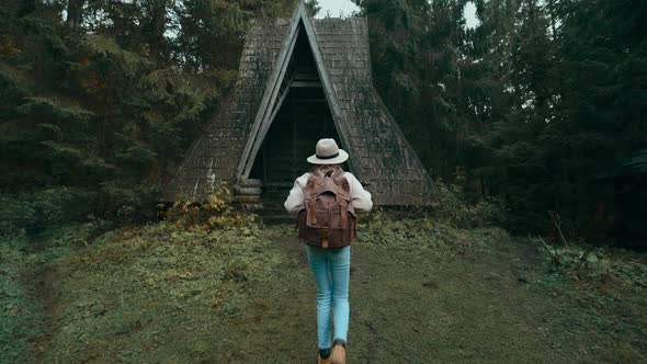 Stylish Tourist Woman in Hat with Backpack Coming in Old Vintage Style Wooden Hut