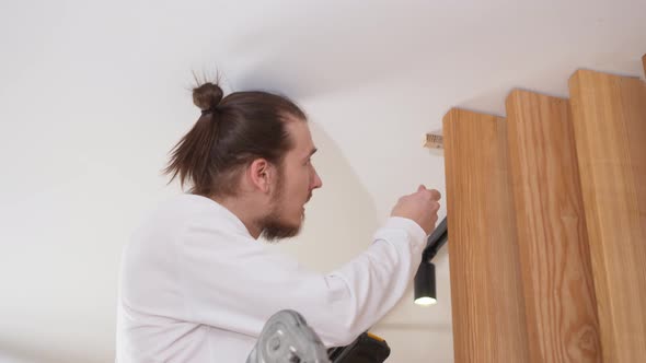 the Carpenter Screws with a Screwdriver Wooden Ash Lamellae to the Ceiling