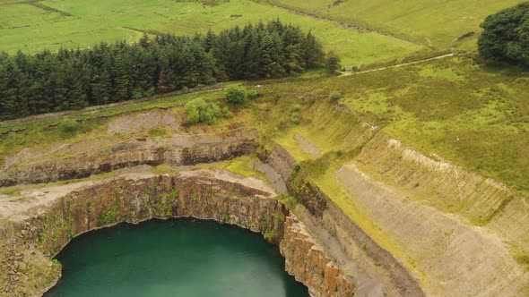 An aerial view over a quarry with a turquoise pond