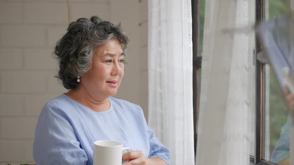 Portrait senior Asian woman drinking tea morning beside a window at home.