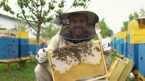 Beekeeper in Protective Workwear Inspecting Honeycomb Frame at Apiary