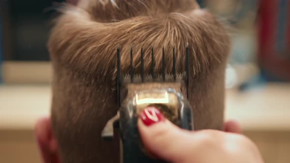 Barbershop, close-up: a female barber cuts a male client's hair. The razor cuts hair.