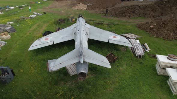 Aerial view descending behind neglected Hawker hunter fighter jet among discarded junk in field