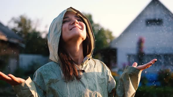 Free Happy Young Woman in Green Raincoat Near Her House Looking Up with Raised Arms Enjoying a Calm