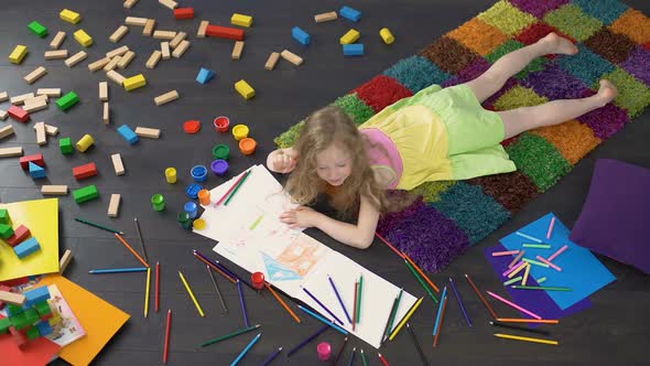 Little Curly Girl Drawing with Color Pencils on The Floor at Home Childhood