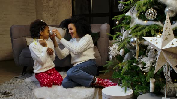 Portrait of Happy African American Mom and Little Daughter Decorate Christmas Tree with Festive Toys
