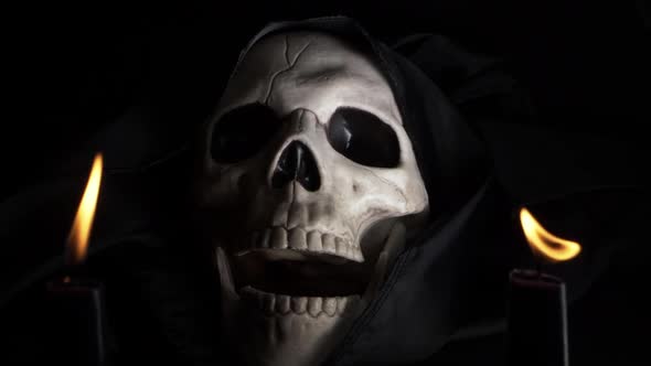 Hooded skull open mouthed with two candles on dark background