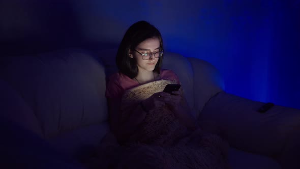 Hapy Girl Sits on the Sofa Near the TV and Uses the Phone in the Evening