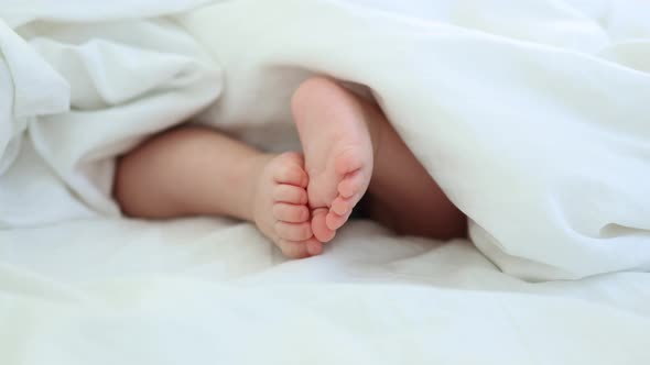 Closeup Bare Feet and Toes of Infant Baby Legs in White Sheet