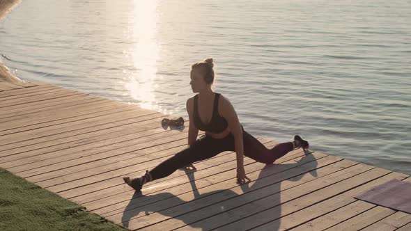 Sporty Young Woman Is Doing Longitudinal Split Sitting on Pier Near River.