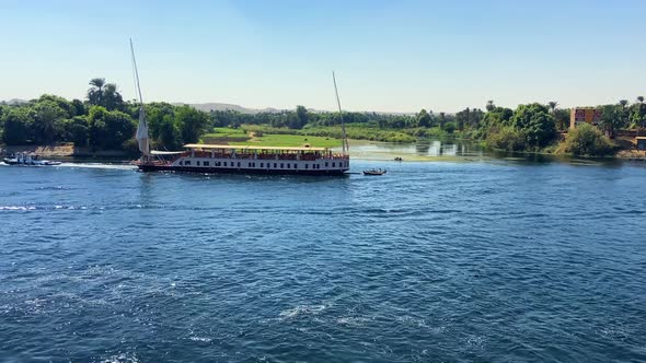 Cinematic video of a large Egyptian cruise boat sailing along the banks of the green Nile River Vall