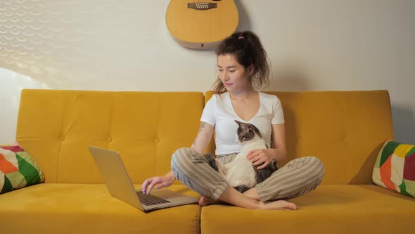 Young Asian Woman Surfing in Internet with Her Cat at Home on Coach