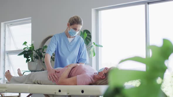 Female health worker massaging hips of senior woman at home