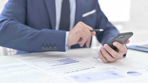 Businessman Using Smartphone for Paperwork