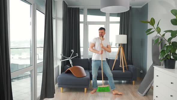 Man Cleaning the House and Having Fun Dancing and Singing with a Broom