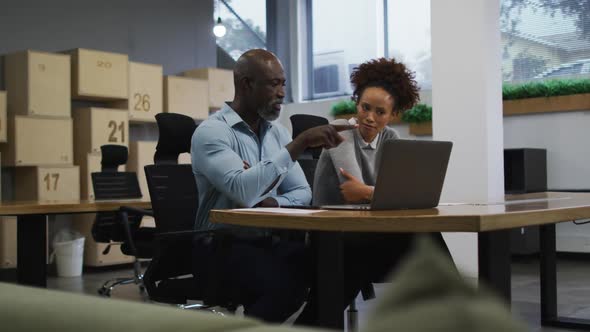 Diverse male and female business colleagues talking and using laptop in office