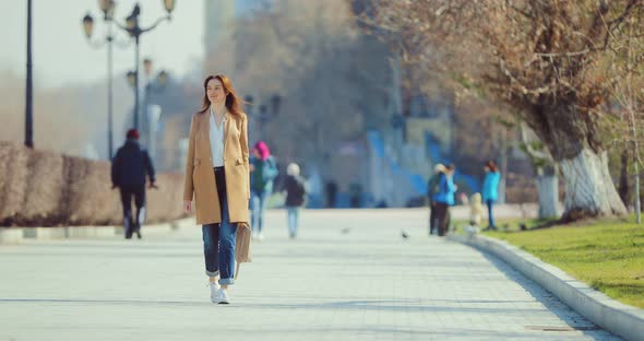 Elegant Young Woman Walks Through the Park in Early Spring