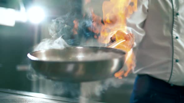 Chef cook cultivates burning alcohol in a frying pan with a lighter for cooking