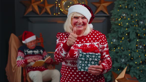 Positive Senior Grandmother in Christmas Sweater Smiling Friendly at Camera and Raises Thumbs Up