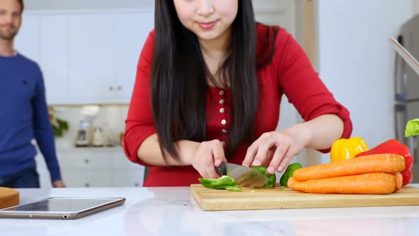 Woman cutting vegetable while interacting with man in kitchen