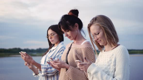 Friendship, Technology and Internet Concept - Three Young Women with Smartphones Outdoors.