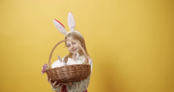 Little Girl Smiles with Rabbit Ears Holds a Basket with a Rabbit in Her Hands